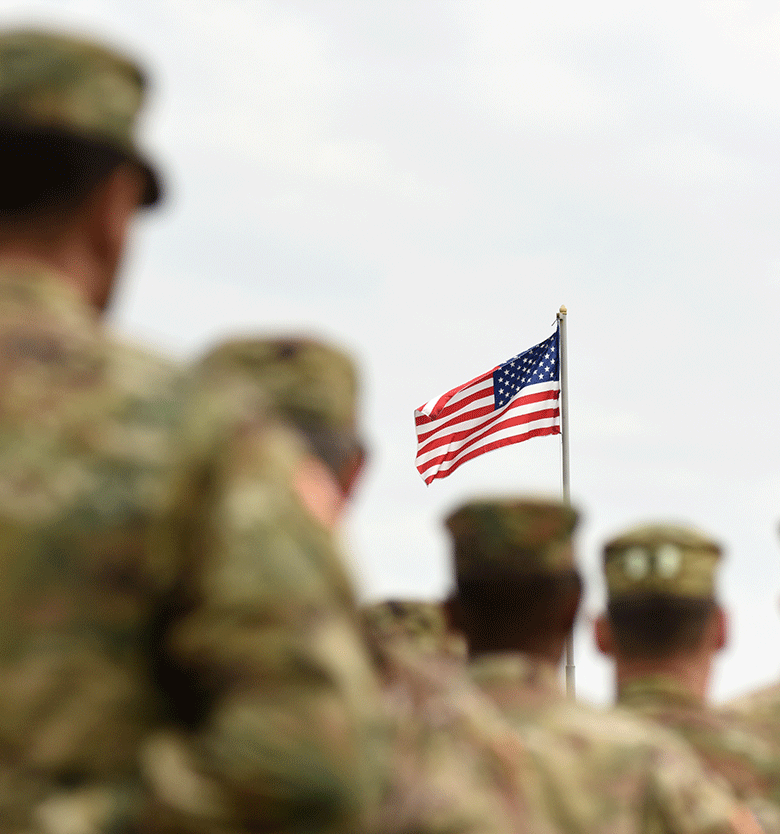 group of soldiers standing at attention while an American flag waves
