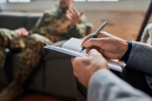 a veteran sitting on a couch shows signs of PTSD as a therapist takes notes in the foreground